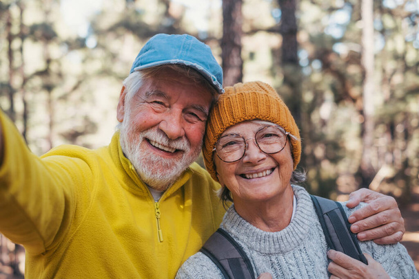 Head shot portrait close up of cute couple of old seniors taking a selfie together in the mountain forest looking at the camera smiling having fun enjoying. Two mature people hiking. - Foto, Imagem