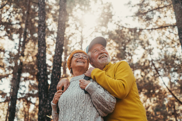 Head shot portrait close up of middle age cheerful people smiling and looking at the the trees of the forest around them. Active couple of old seniors hiking and walking together in the mountain having fun. - Foto, Imagen