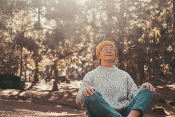 Head shot portrait close up of one middle age old woman resting and relaxing doing yoga in the forest of mountain in the nature. One mature female person enjoying having fun lifestyle. - Photo, image