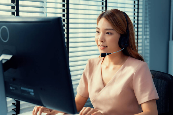 Competent female operator working on computer and while talking with clients. Concept relevant to both call centers and customer service offices. - Photo, Image
