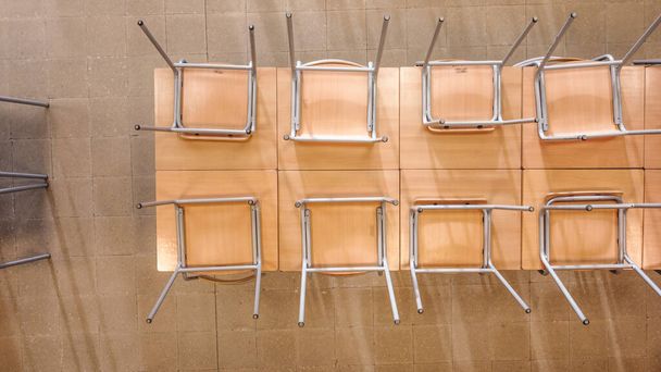Top view of similar upside down chairs placed on wooden table in light classroom in school after classes - Foto, Bild