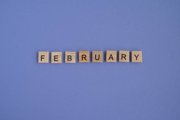 The name of the month FEBRUARY is written on wooden cubes isolated. Very Peri Color of the Year background, copy space. Top view of wooden blocks with letters. Step by step, step 2. - Foto, Imagen