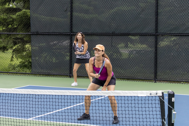 Two pickleball players prepare to return a ball on a suburban pickleball court during summer. - Photo, image