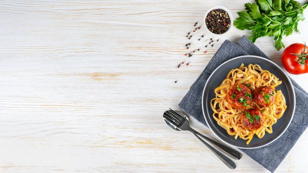 Kotitekoinen spagetti tomaattikastikkeella lihapullia ja mausteita tarjoillaan valkoisella taustalla. Maukasta kypsennettyä pastaa ja lihapullia, jotka on valmistettu jauhelihasta, elintarvikkeiden ainesosista. Top View, Litteä lay, banneri, kopioi tilaa - Valokuva, kuva