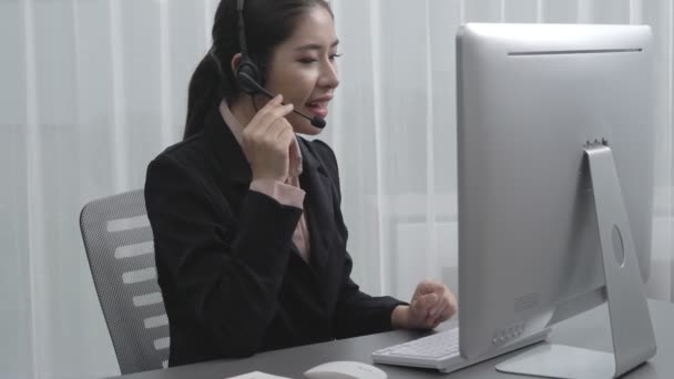 Asijská zákaznická podpora operátor nosí sluchátka a mikrofon pracuje u svého stolu s notebookem. Nadšená žena zaměstnanec poskytovat zákaznický servis, podpůrné call centrum agent pomáhá zákazníkům. - Záběry, video