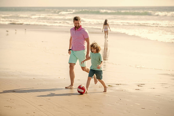 Ojciec i syn grają w piłkę na plaży. Tatuś z małym chłopcem w upalny letni dzień. Dzień rodziny w weekend. Tata i dziecko bawią się na świeżym powietrzu. Dzieciństwo i rodzicielstwo. rodzinne wakacje. aktywność sportowa. - Zdjęcie, obraz