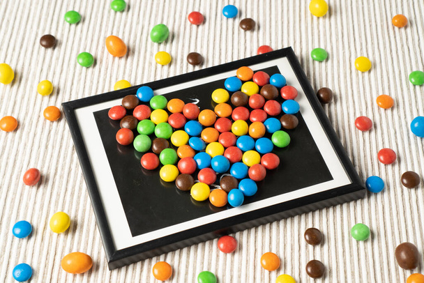 A playful and fun design with small dragee candies arranged like a picture in a frame on a white table. - Valokuva, kuva