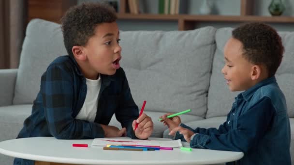 Two ethnic African American multiracial multiethnic boys kids schoolboys pupils sons siblings indoors at home children brothers cousins friends draw picture together talking playful drawing hobby game - Video, Çekim
