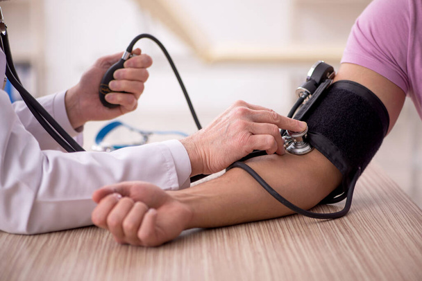 Médico viejo midiendo pacientes jóvenes presión arterial - Foto, Imagen