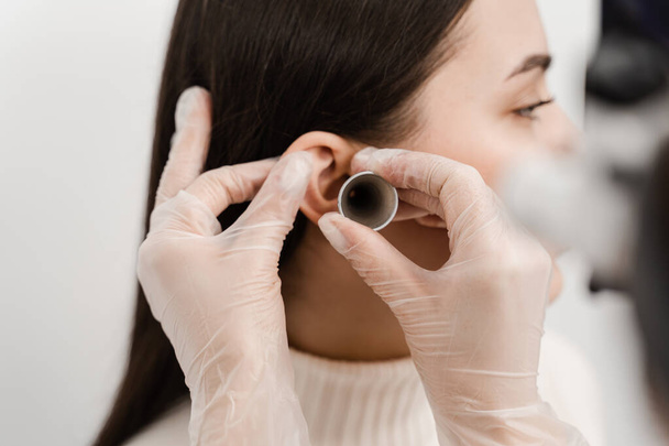 Крупный план женского уха с воронкой в ухе. Оттоскопия. Посещение ЛОР-врача и консультации - Фото, изображение