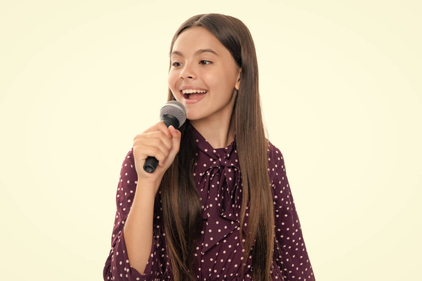 Dětský zpěv. Emocionální ohromený dospívající dívka s mikrofonem zpívající na bílém pozadí. Zpívající krásná zpěvačka dívka držet mikrofon - Fotografie, Obrázek