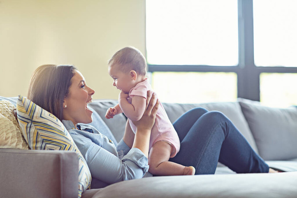 Woman, bonding and laughing mother with baby girl on house living room, relax nursery and family home sofa. Smile, happy and infant child with mom in comic, funny or silly children game in trust love. - Photo, image