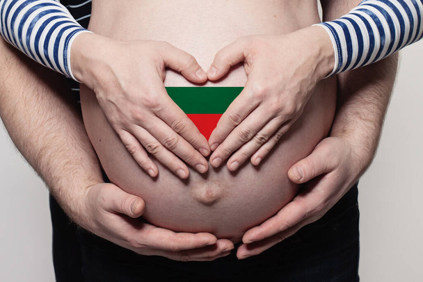 Bulgarian family concept. Man embracing pregnant woman belly and heart with flag of Bulgaria colors closeup - Foto, afbeelding