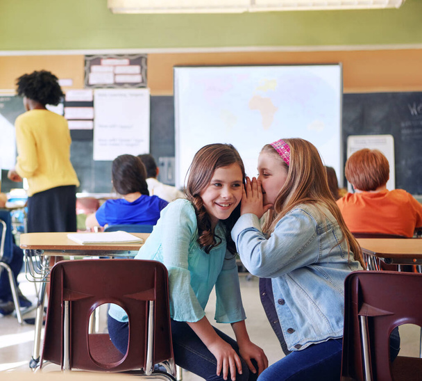 Student, friends and whisper in classroom for secret, gossip or chatting during teaching lesson. Sneaky young female learners sharing quiet information secretly in ear at class while teacher is busy. - Foto, imagen