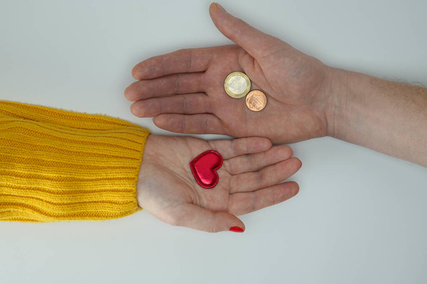 Love for money, selling love. Two hands, male and female, extend their palms to each other. In one hand is a red heart, in the other hand are coins. Close-up. Isolated on white background. - Foto, Bild