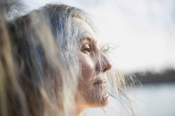 Close up woman with half closed eyes and silver hair falling on face portrait picture. Closeup side view photography with blurred background. High quality photo for ads, travel blog, magazine, article - Foto, imagen