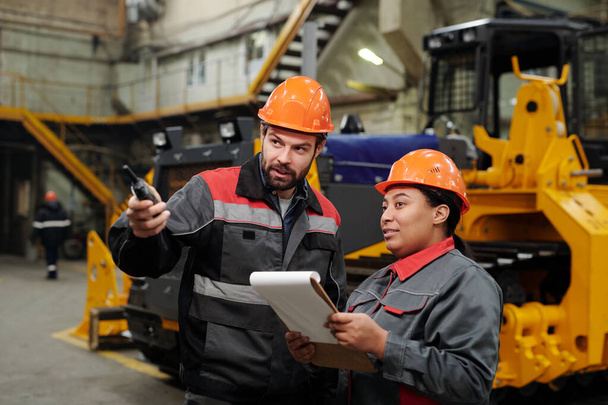 Two interracial workers of industrial plant discussing new equipment for machinery production while foreman pointing forwards - Foto, imagen