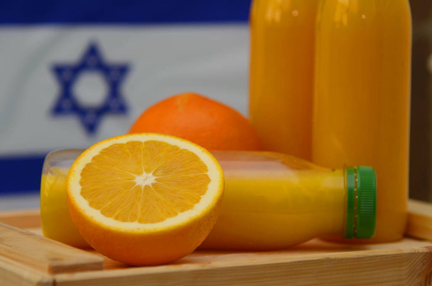 Plastic bottle with fresh juice. The flag of Israel is in the background. Concept: Israeli orange juice, Middle Eastern oranges - Foto, afbeelding