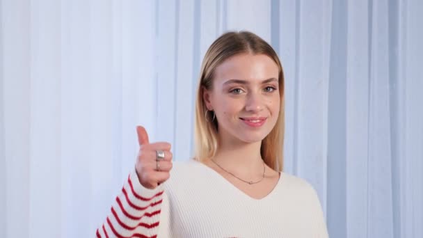 Confident happy smiling young girl teen student wears casual cool sweater showing thumb up. Satisfied woman looking at camera giving positive service or goods recommendation, approval symbol - Felvétel, videó