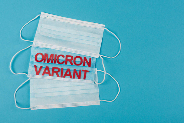 Top view of medical masks with omicron variant lettering on blue background  - Foto, Imagem