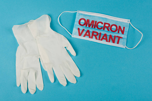 Top view of latex gloves near medical mask with omicron variant lettering on blue background  - Fotó, kép
