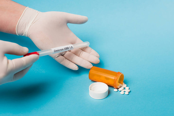 Cropped view of doctor in latex gloves holding throat swab with omicron lettering near pills on blue background  - Foto, afbeelding