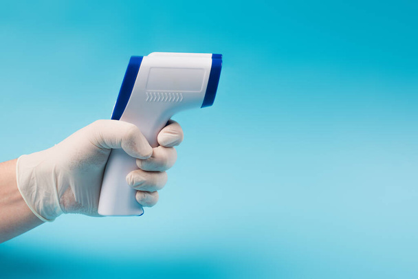 Обрізаний вид лікаря в латексних рукавичках, що тримає пірометр ізольовано на синьому
  - Фото, зображення
