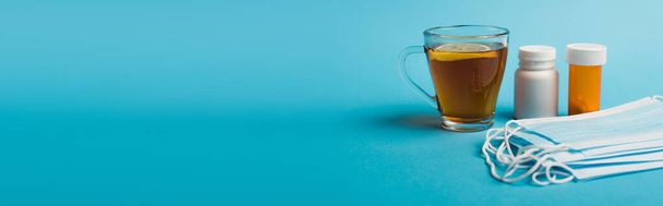 Medical masks near pills and cup of tea with lemon on blue background, banner  - Zdjęcie, obraz