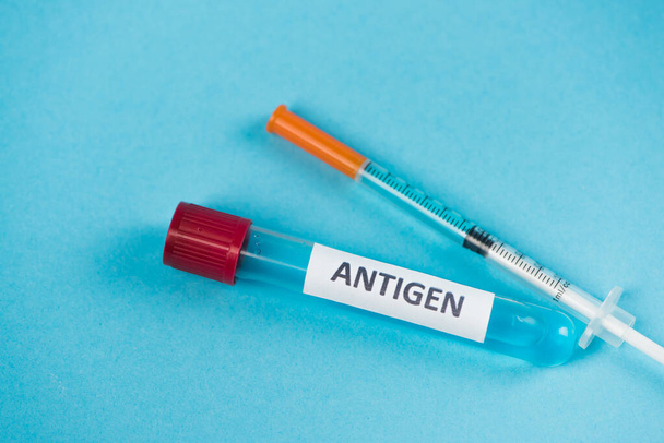 Close up view of syringe and test tube with antigen lettering on blue background  - Foto, afbeelding
