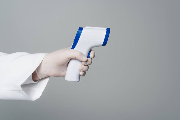 Обрізаний вид лікаря в латексній рукавичці, що тримає безконтактний пірометр ізольований на сірому
  - Фото, зображення