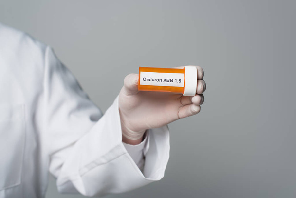 Cropped view of doctor in latex glove holding pills with omicron xbb lettering isolated on grey  - Foto, afbeelding