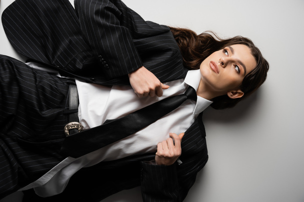 top view of young woman looking away while lying in stylish formal wear on grey background - Foto, Bild