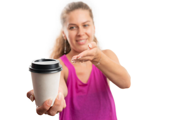 Взрослая женщина, улыбающаяся в розовом тренажерном зале для тренировки, представляет крупный план бумажной чашки кофе в качестве утренней фитнес-концепции, изолированной на белом фоне студии - Фото, изображение