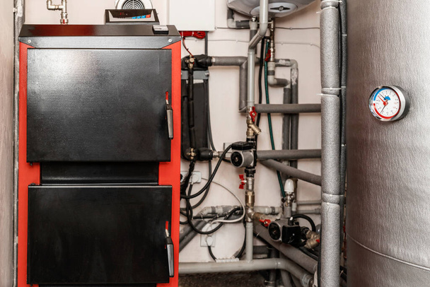 パイプ、バルブ、循環ポンプ、ハウスボイラー室内の貯蔵タンクを備えた固体燃料ボイラー。現代のエコン温水暖房システム - 写真・画像