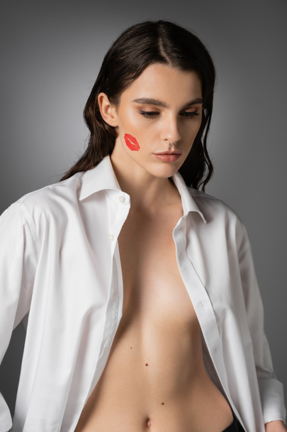 sexy woman with red lip print on face posing in white unbuttoned shirt on grey  - Foto, immagini
