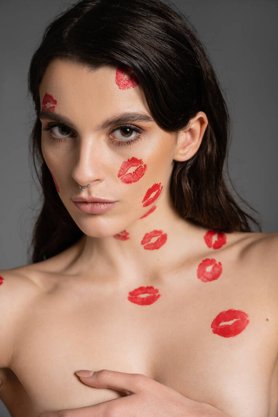 sexy shirtless woman with red lip prints covering breast with hand while looking at camera isolated on grey - Foto, Imagen
