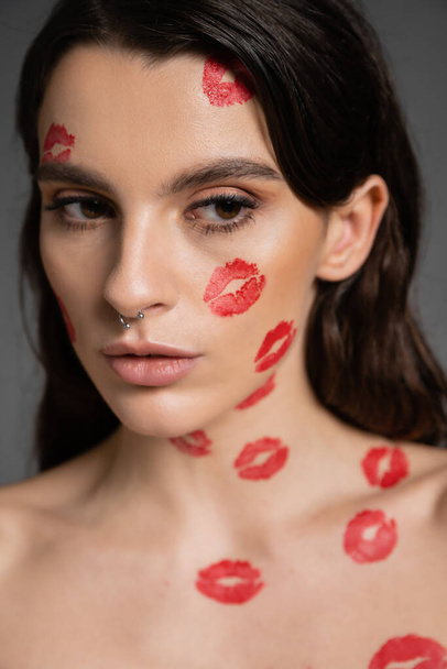 portrait of pretty brunette woman with red kiss prints on face and body isolated on grey - Foto, imagen