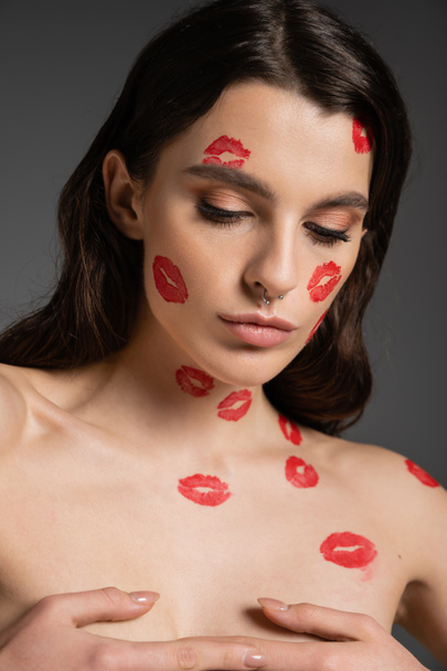sensual shirtless woman with red kisses on body and face covering breast with hands isolated on grey - Photo, image