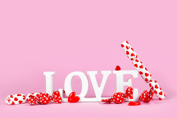 White wooden word LOVE with candy with hearts on pink background with copy space - Fotografie, Obrázek