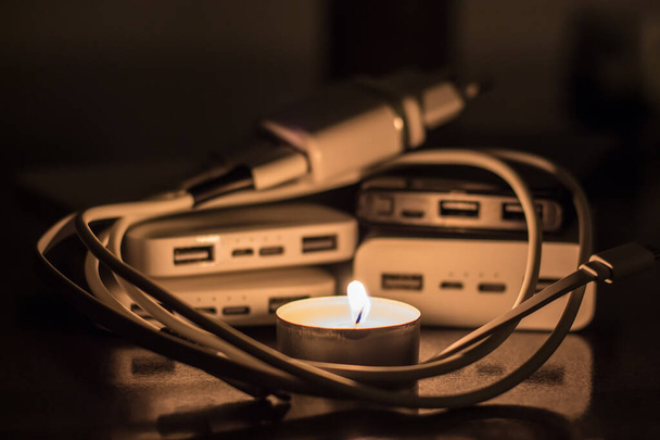 A burning candle against the background of power banks and a charger. Blackout due to war in Ukraine - Φωτογραφία, εικόνα