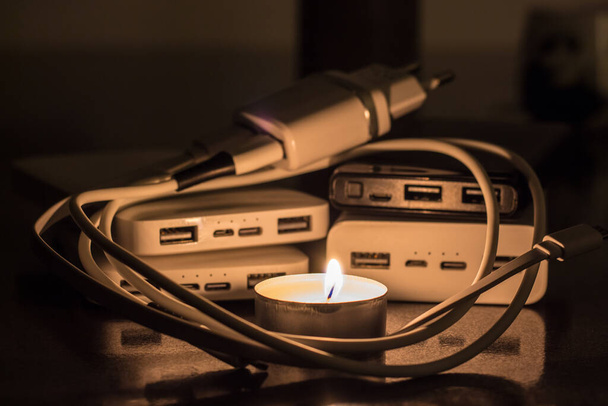 A burning candle against the background of power banks and a charger. Blackout due to war in Ukraine - Fotoğraf, Görsel