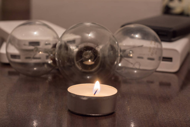 A burning candle against the background of lamps and power banks. Blackout due to war in Ukraine - Foto, imagen