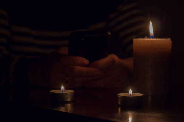 Mobile phone in hands and burning candles. Blackout due to war in Ukraine - Foto, afbeelding