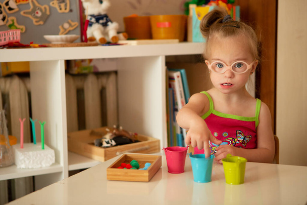 A beautiful smart girl with Down syndrome learns to sort by colors. Multicolored figures - Foto, Imagem