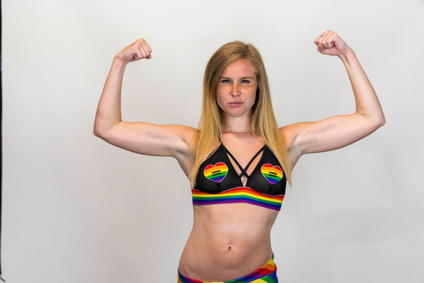 Studio image of happy young blonde LBGTQ woman wearing rainbow colored clothes smiling at camera.  Concept of homophobia, diversity, equity, peace and love, freedom, liberty. LGBT rights concept.   - Photo, Image