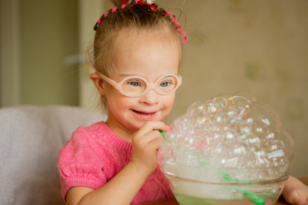 A beautiful little girl with Down syndrome learns to blow soap bubbles. Blow through a tube. Speech therapy exercises - Zdjęcie, obraz