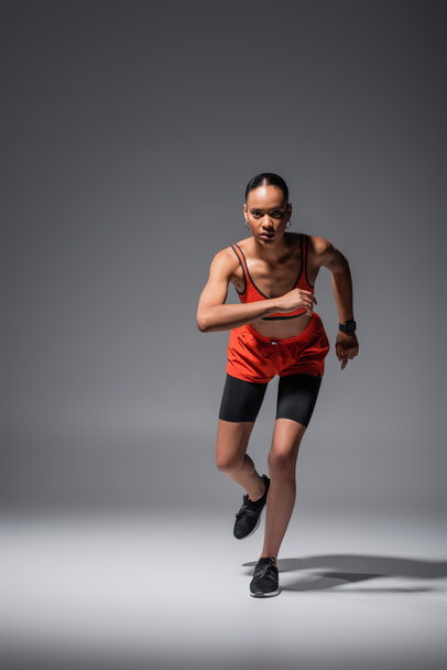 full length of young african american sportswoman in sneakers running on grey  - 写真・画像
