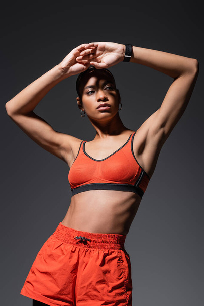 young african american sportswoman in red sports bra posing with raised hands isolated on grey  - Φωτογραφία, εικόνα