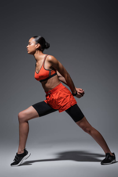 full length of brunette african american woman in sportswear and sneakers exercising on grey  - Fotó, kép