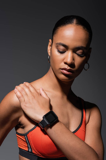 brunette african american woman with fitness tracker posing isolated on grey  - Фото, изображение